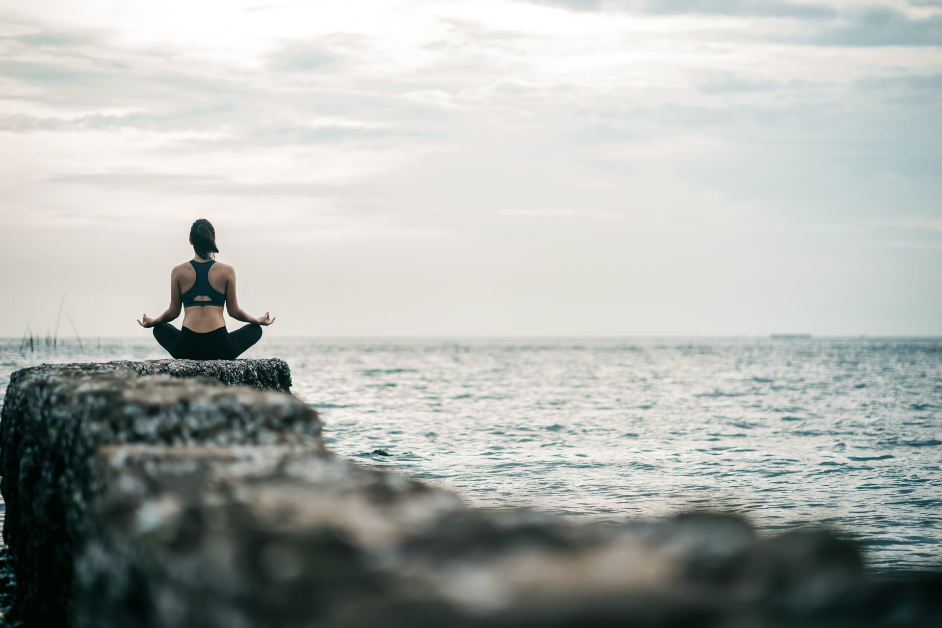 Young Asian woman practicing yoga exercise at quiet rock pier with sea background. Sport and recreation in city rush.